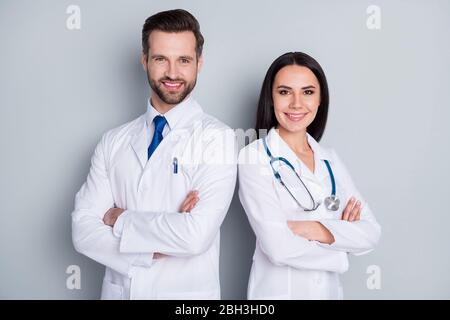 Photo of handsome doc guy lady patient consultation virology clinic stand back-to-back toothy smiling arms crossed experienced doctors wear lab coats Stock Photo