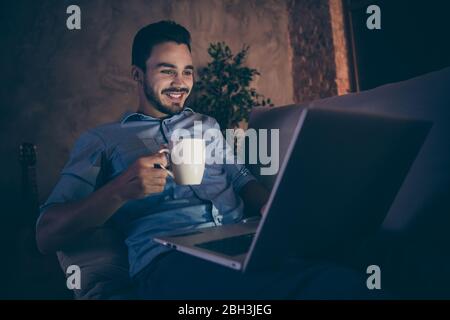 Portrait of his he nice attractive focused confident cheerful cheery brunet guy sitting on divan using laptop late night at modern loft industrial Stock Photo