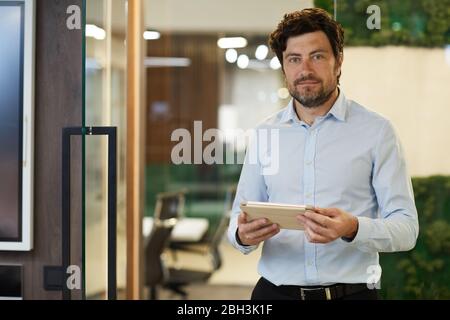 Portrait of bearded businessman looking at camera while using tablet pc at office Stock Photo