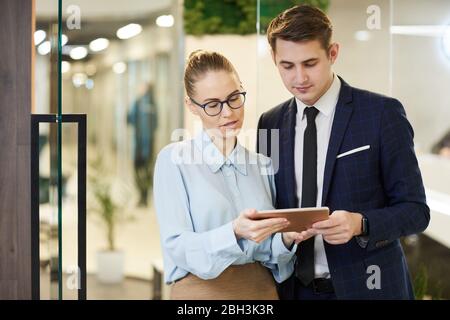 Young business couple watching something on digital tablet together while standing at office Stock Photo