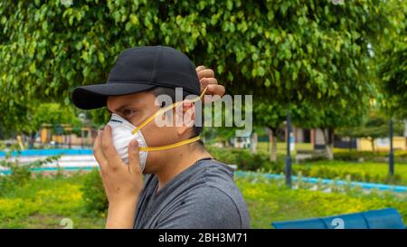 Close up view of latin man on the street putting on a white face mask using both hands Stock Photo