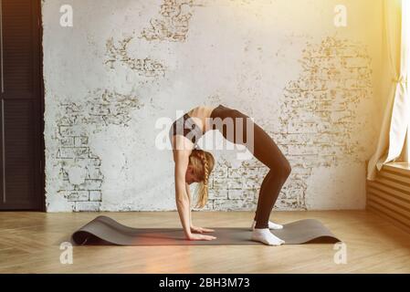 Lovely young girl goes in for sports at home in a sports uniform on a rug. Sport, beautiful young woman practicing yoga, doing bridge pose, standing in Urdhva Dhanurasana, working out wearing sportswear Stock Photo