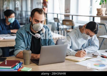 Photo of multinational focused students in medical masks studying with laptop at classroom Stock Photo
