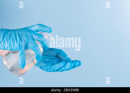 Female hand in latex surgical gloves is using antiseptic hand sanitizer, blue background. Alcohol based sanitizer gel for hand hygiene protect from Stock Photo