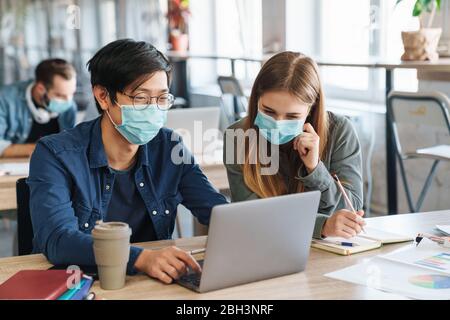 Image of multinational joyful students in protective mask talking while studying with laptop at classroom Stock Photo