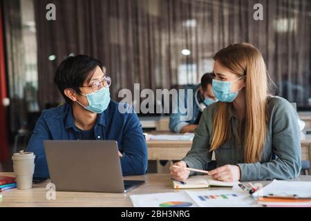 Image of multinational young students in protective mask talking while studying with laptop at classroom Stock Photo