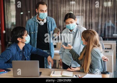Image of multinational joyful students in protective mask talking while studying with laptop at classroom Stock Photo