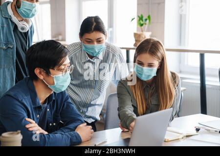 Image of multinational serious students in protective mask talking while studying with laptop at classroom Stock Photo