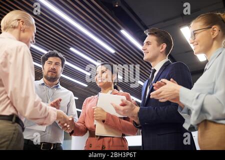 Two businesswomen shaking hands to each other they concluding a deal while other people standing and clapping Stock Photo
