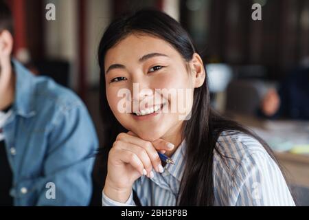 Photo of asian cheerful student in casual wear smiling and looking at camera while studying at classroom Stock Photo