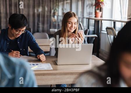 Photo of multinational young students using laptop and smartphone while studying at classroom Stock Photo