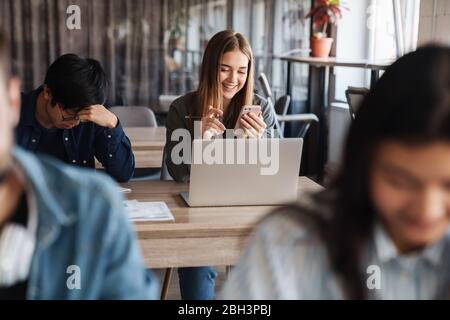 Photo of multinational young students using laptop and smartphone while studying at classroom Stock Photo