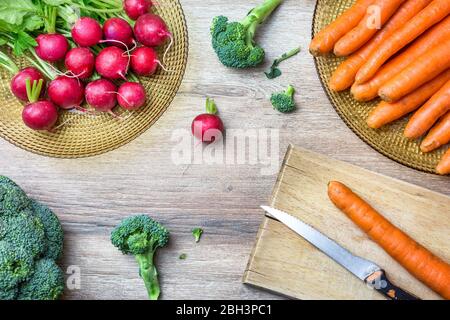 Fresh organic red radishes, carrots and broccoli on wooden background. Top view with copy space. Healthy nutrition concept.