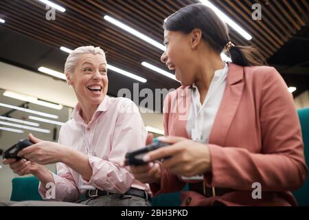 Excited business colleagues sitting with joysticks and playing in video game at office Stock Photo