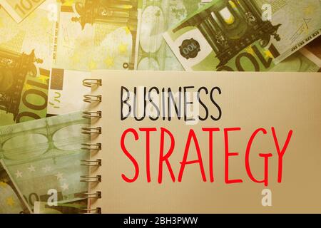 Business Strategy words written on copybook page on Hundred Euro bills banknotes background. Strategical management Concept Stock Photo