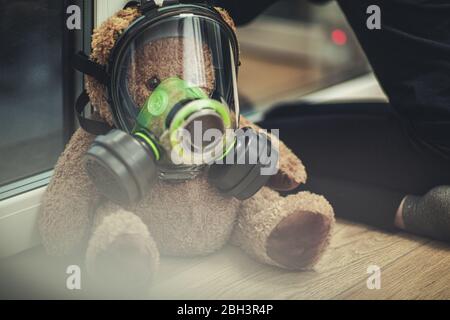Girl Looking Out The Bedroom Window With Teddy Bear Wearing Gas Mask. Stock Photo