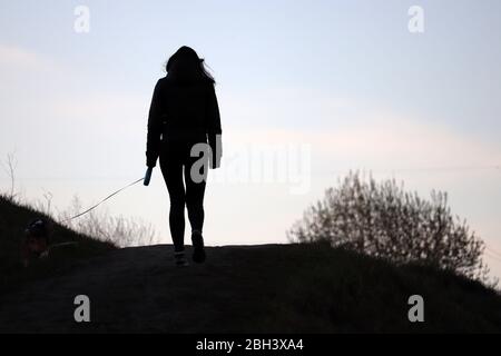 Silhouette of a girl walking a dog on a leash on a hill. Care for a pet during coronavirus pandemic, spring weather Stock Photo