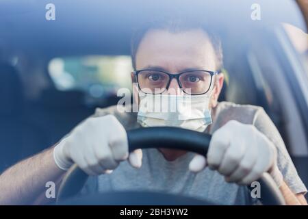Close up of driver in protective mask with hands in rubber gloves on steering wheel, covid-19 protection from bacteria and virus infection. Stock Photo