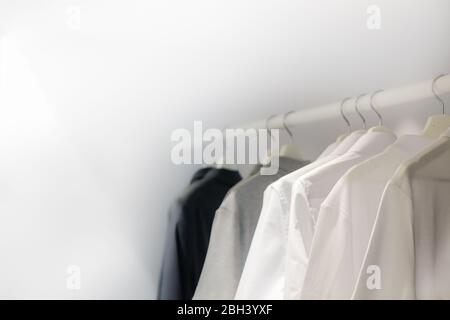 Row of white t-shirts on hangers on rack Stock Photo by FabrikaPhoto