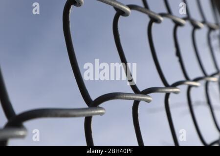 Closeup perspective view of a section of chain link fence against a blue sky, bokeh effect Stock Photo