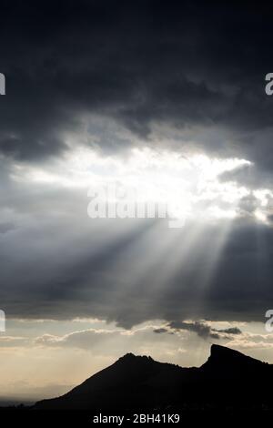 Sunbeams appearing between the dark storm clouds over the mountain Stock Photo