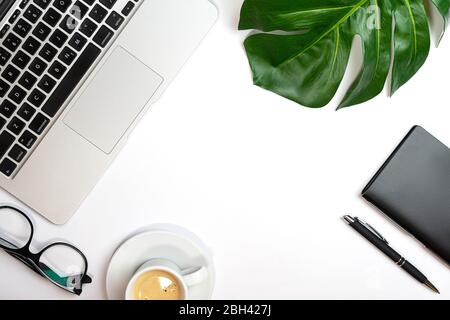 Top view of white office desk with laptop, notebook, palm leaf, cup of coffee and supplies. Working from home concept. Top view with copy space. Close up. Stock Photo