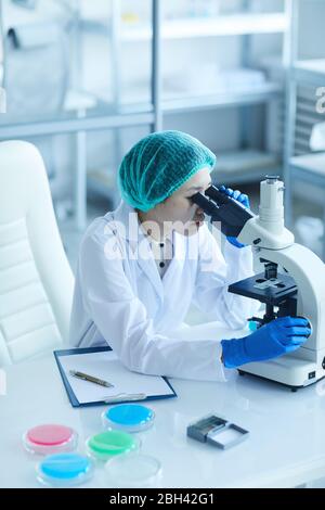 Female scientist sitting at her workplace and examining samples using microscope in the laboratory Stock Photo