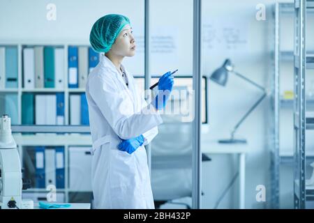 Pensive female doctor in white coat standing at the office and thinking about something Stock Photo