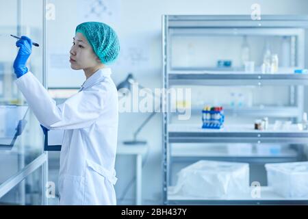 Female doctor in white coat standing against the glass wall and making notes on it at hospital Stock Photo