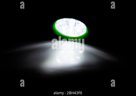 Green LED torch shining a light on a white surface in a darkened room Stock Photo