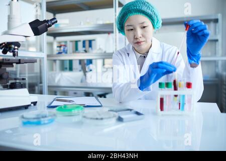 Asian female doctor sitting at her workplace and working with blood samples in test tubes in the laboratory Stock Photo