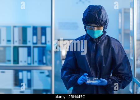 Doctor in protective costume and in mask examining the samples while working in the laboratory Stock Photo
