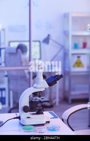 Close-up of microscope standing on the table with people working in the background at laboratory Stock Photo