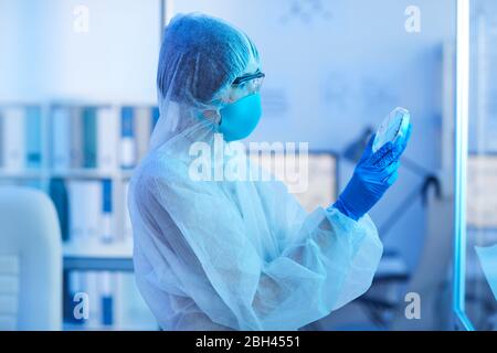 Medical worker in protective costume looking at samples in her hands while standing at medical laboratory Stock Photo