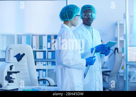 Two scientists in white coats discussing scientific experiment together while working at the laboratory Stock Photo