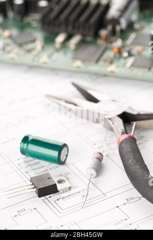 Transistor, resistor and capacitor electronic parts or components with pliers in front of pcb board with pcb wiring diagram - electronic device repair Stock Photo