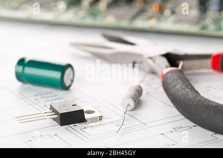 Transistor, resistor and capacitor electronic parts or components with pliers in front of pcb board with pcb wiring diagram - electronic device repair Stock Photo