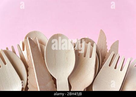 Eco cutlery from pine wood. Disposable tableware from natural materials. Wooden spoon, fork and knife agains a pink background. Stock Photo