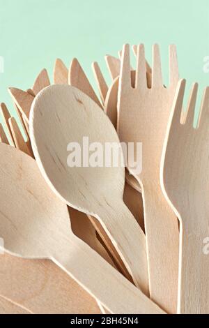 Eco cutlery from pine wood. Disposable tableware from natural materials. Wooden spoon, fork and knife agains a green background. Stock Photo