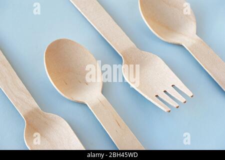 Eco cutlery from pine wood. Disposable tableware from natural materials. Wooden spoons and forks in a row on a blue background. Stock Photo