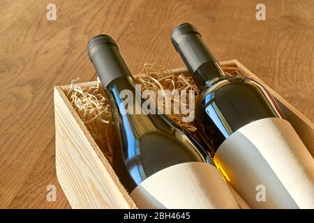 Bottles of red and white wine in wooden gift box with straw. Glass bottles with blank labels for use as mockup or template. Stock Photo