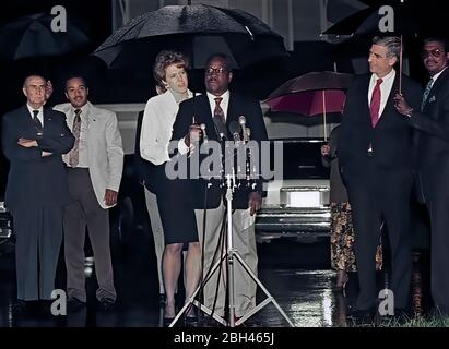 Alexandria Virginia, USA October 15, 1991 Mrs, Virginia Thomas wife of now Associate Justice of the United States Supreme Court, Clarence Thomas stands behind Thomas at the microphones for a short news conference under umbrellas during a rain shower to acknowledge the vote of the Senate Judiciary Committee confirming his nomination as Associate Judge to the Court. On the far left is Senator Strom Thurmond (Republican of South Carolina) and on the far right is Senator John Danford (Republican of Missouri) Stock Photo