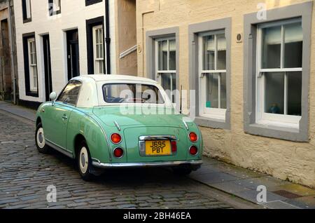 the retro 1960's looking car, the  Nissan Figaro parked on a cobbled street in the old town of St andrews, fife, Scotland Stock Photo
