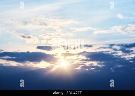 Setting sun is behind the clouds, and rays of light are breaking through the clouds Stock Photo