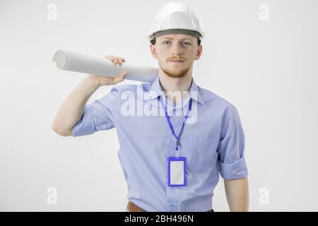 confident young businessman in white helmet holds rolled-up drawing on shoulder Stock Photo