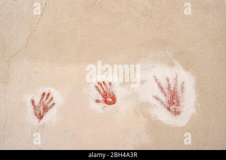 Red handprints on the wall. Two children's handprints and one adult handprint on a stone wall Stock Photo