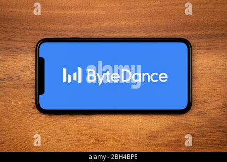 A smartphone showing the Bytedance logo rests on a plain wooden table (Editorial use only). Stock Photo