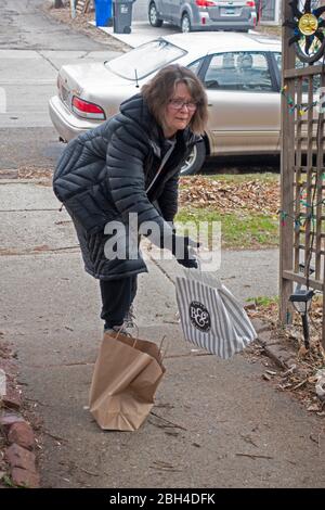 Neighbor exchanging bags of food and reading materials at social distance on sidewalk of home during the Covid-19 pandemic. St Paul Minnesota MN USA Stock Photo