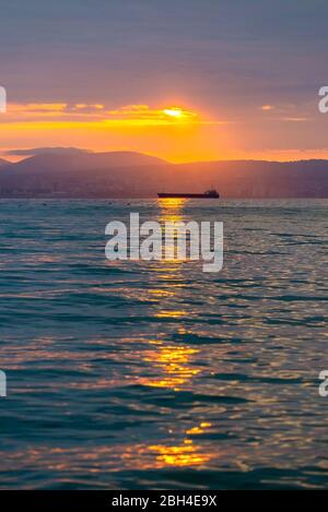 Cargo ship sailing the sea at a golden sunset or sunrise. Ocean shipment across water as the sun sets or rises. Harmony and beauty in nature. Scenic p Stock Photo