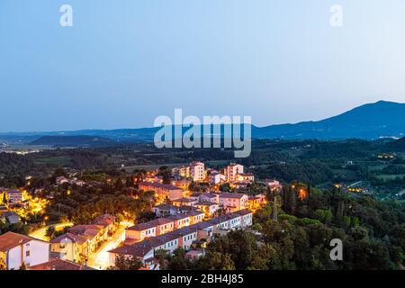 Chiusi town village at night in Tuscany, Italy with illuminated lights on streets and rooftop houses on mountain countryside and rolling hills Stock Photo
